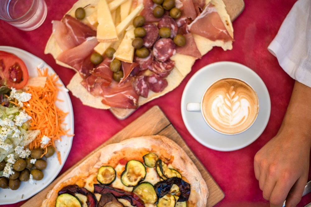 A fresh pizza, plate of cured meats and cheese and a coffee