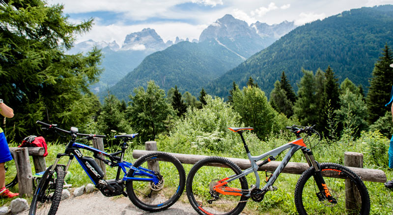 Two mountain bikes rest on a fence with a view of mountains and greenery behind - Dolomites, Italy