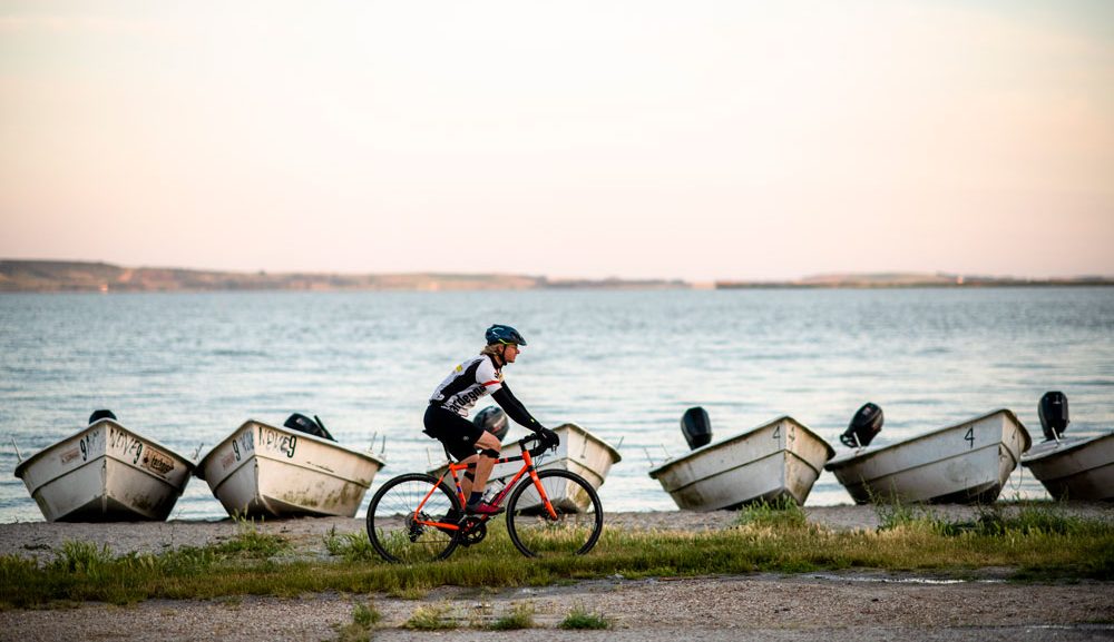 A cyclist rides past small boats at sunset