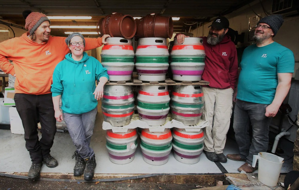 A group of Brewers stand in front of kegs at the First and Last Brewery