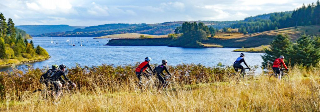 A group of cyclists ride off road alongside Kielder Water