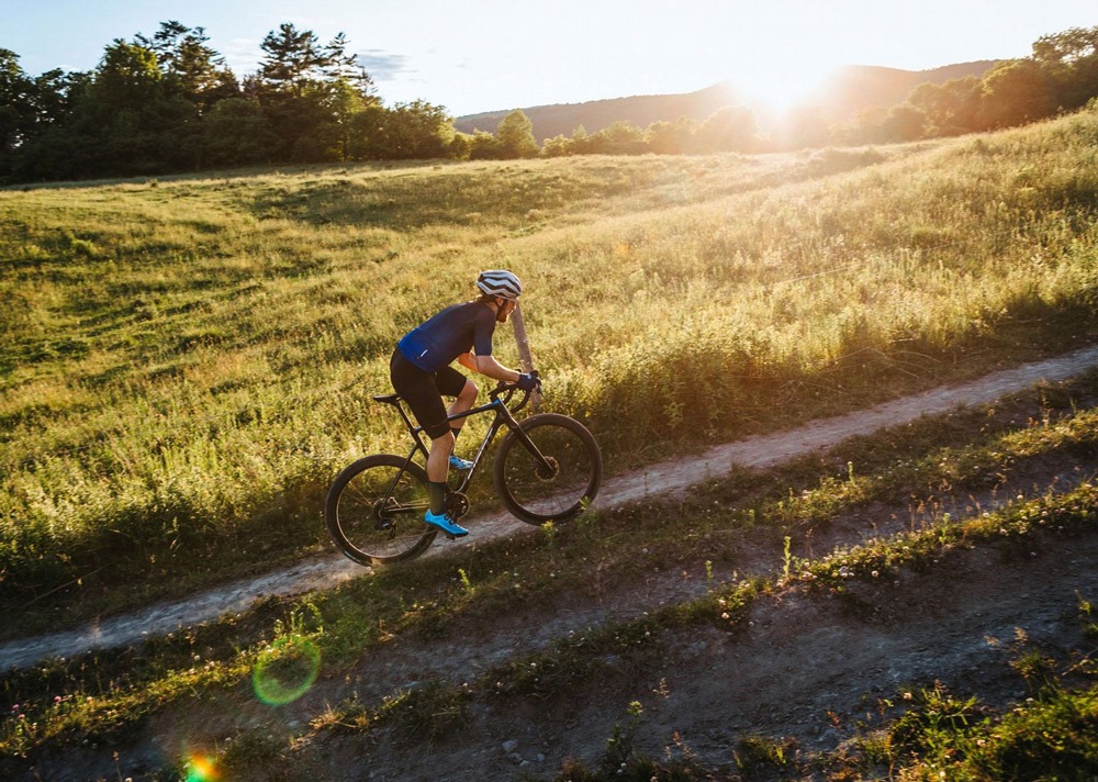 A gravel cyclist rides up a grassy hill at sunset