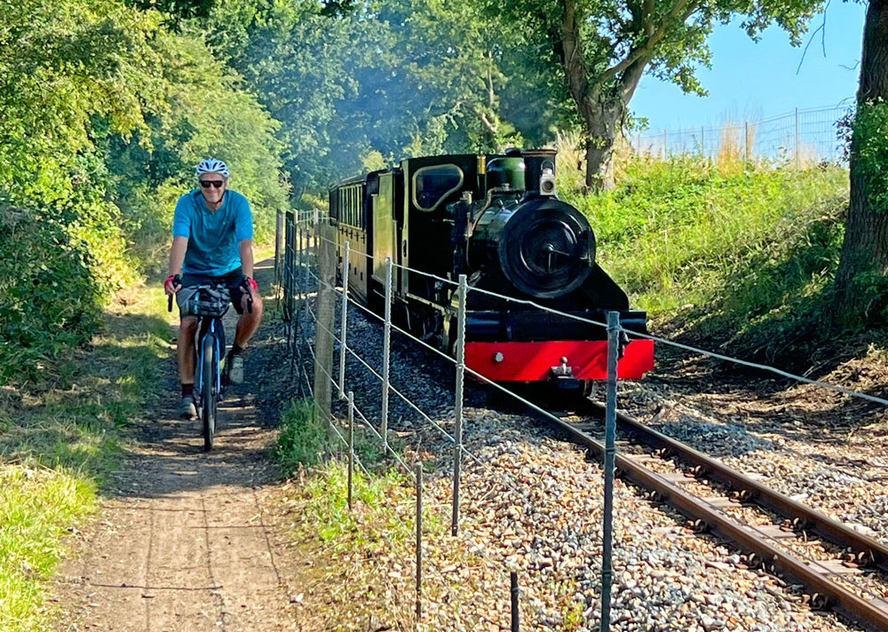 Cyclist rides alongside a small black and red steam train