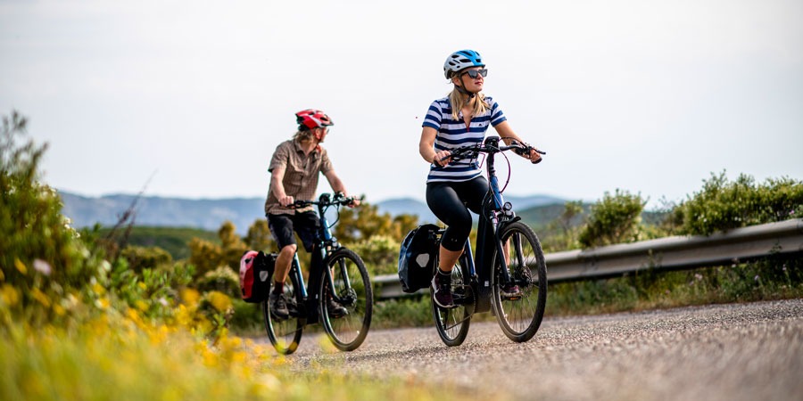 Two people ride up a hill in the countryside on e-bikes