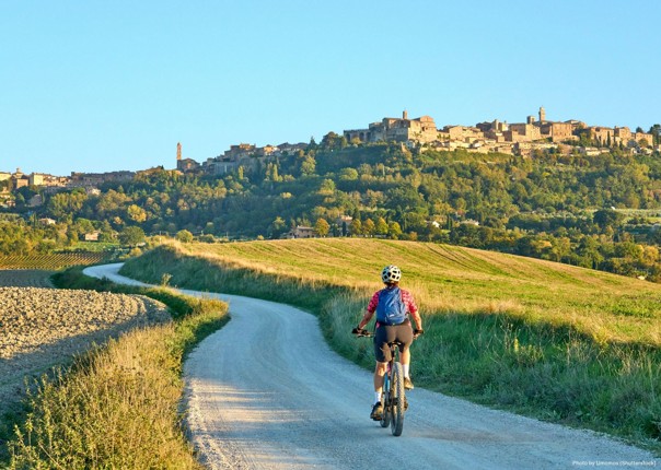 Woman mountain biking in Tuscany towards a town