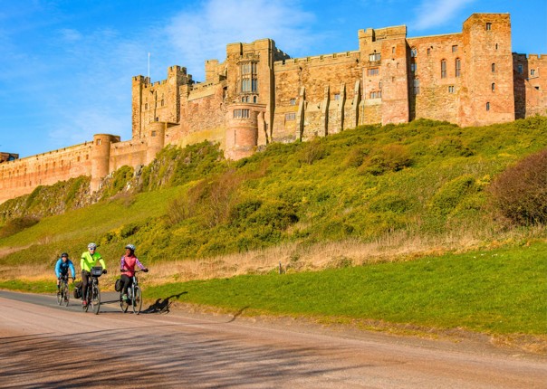 Cyclists riding past Bamburgh Castle