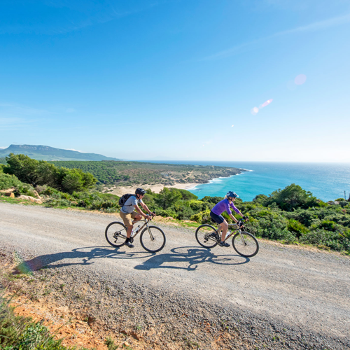 Two cyclists on a sunny coastal gravel track in spain